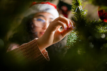 Close up of woman decorating a Christmas tree, surrounded by lush greenery and festive beads, exuding calmness and holiday cheer in a close and intimate setting.