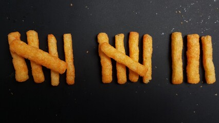 Crispy golden snack sticks neatly arranged in groups to resemble tally marks on a dark background, symbolizing counting with food.  
