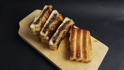 Toasted bread sandwiches filled with melted chocolate stacked on wooden board, creating a warm, sweet, and indulgent snack.  
