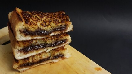 Toasted bread sandwiches filled with melted chocolate stacked on wooden board, creating a warm, sweet, and indulgent snack.  
