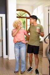 Young diverse couple enjoying coffee break while unpacking boxes in new home