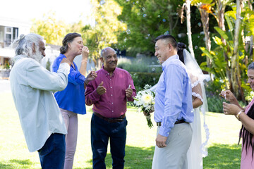 Blowing bubbles at joyful senior wedding party, diverse group celebrating outdoors