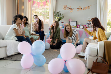 Women celebrating baby shower with balloons and laughter in cozy living room