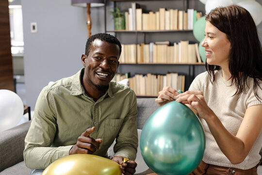 Inflating colorful balloons, friends celebrating festive occasion at home together - Powered by Adobe