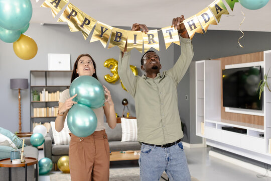 Preparing living room for celebration, friends decorating with birthday banner - Powered by Adobe