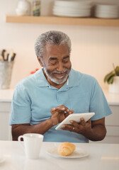 Elderly man enjoying breakfast while using tablet at home kitchen table