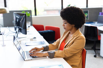 Focused woman typing on laptop at modern office desk, working on project