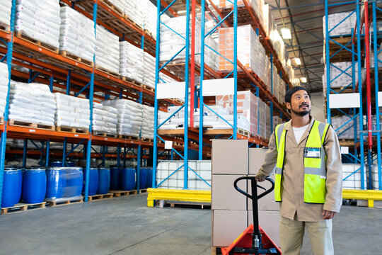 Warehouse worker moving boxes with pallet jack, organizing inventory efficiently, copy space