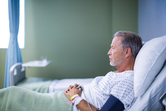 Elderly man resting in hospital bed, looking thoughtful and relaxed, copy space