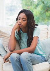 Obraz premium Thoughtful woman sitting on couch at home, looking pensive and relaxed