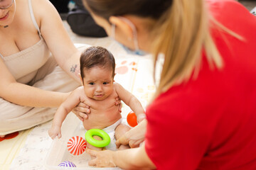 Aquatic therapy for premature baby held by Latina mother, guided by physiotherapist in clinic with...