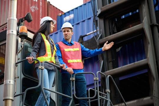 Two workers in safety vests and helmets on a forklift in a cargo port setting, focused and communicative at container yard