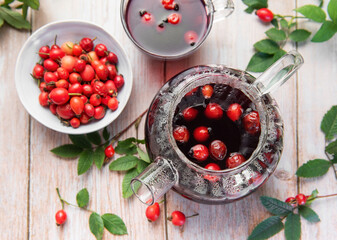Steaming rosehip tea brewing in glass teapot with fresh rosehips
