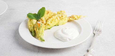 fried zucchini flowers with ricotta on white plate with yogurt on white table