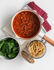 Ingredients for cooking lunch - bolognese sauce, pasta, spinach on a light background, top view