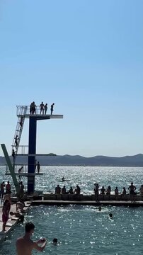 group of people jumping off diving platform against clear blue sky on a sunny day at a beach in Zadar, Croatia