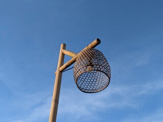 Wooden post with a woven bamboo lamp against a clear blue sky.