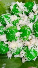 Close-up of Klepon, traditional Indonesian sweet rice cakes. Green glutinous rice balls are covered with grated coconut and served on a banana leaf