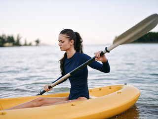 Young woman kayaking on calm water wearing navy blue outfit, focused and sporty, outdoor activity with peaceful lake background