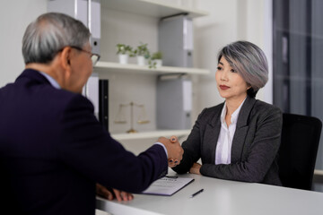 Experienced Asian legal professionals finalize contract with handshake demonstrating trust commitment successful partnership in modern office