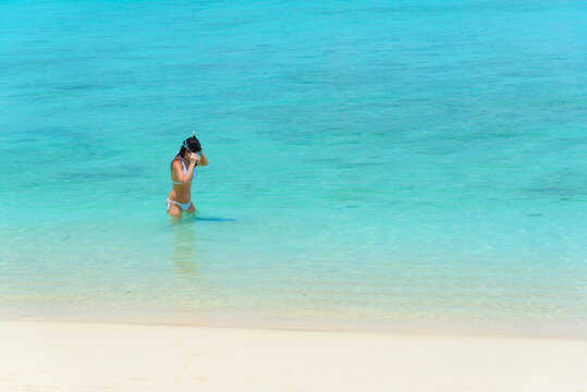 A female tourist in white bikini is enjoying beach holiday, putting on a snorkeling mask and getting ready to snorkel in the bright blue water under the sun, copy space, Koh kradan, Trang, Thailand.