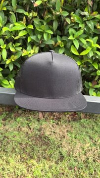 Black trucker cap mockup on outdoor with green leaves background for fashion and branding design zoom in camera movement
