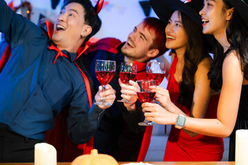 Happy friends in witch and devil costumes celebrating Halloween with drinks, pumpkins, pizza, and laughter at a festive indoor party.