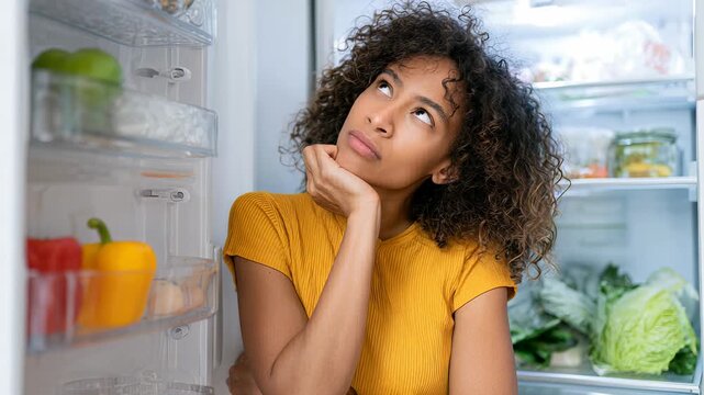 Pensive African American Woman Looking into Refrigerator for Healthy Food Choices, Meal Planning and Grocery Shopping Inspiration