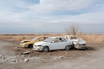 Abandoned cars on desolate landscape near lake under cloudy sky