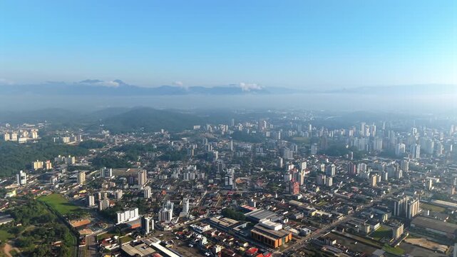 A stunning aerial view of Joinville, Santa Catarina, Brazil, as the city wakes up under a blanket of morning fog. This beautiful shot captures the cityscape at sunrise.
