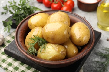 Tasty young boiled potatoes with dill and oil in bowl on grey table, closeup