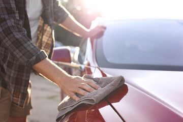 Man wiping car with grey microfiber rag outdoors, closeup
