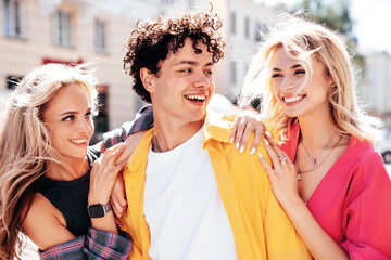 Group of young three stylish friends posing in the street. Fashion man and two cute female dressed in casual summer clothes. Smiling models having fun. Cheerful women and guy outdoors
