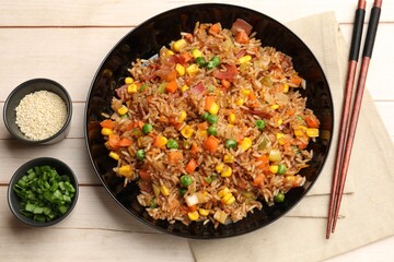 Tasty fried rice and chopsticks on light wooden table, flat lay