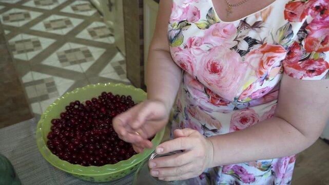 putting cherries in jars, a woman is preparing cherry compotes in jars
