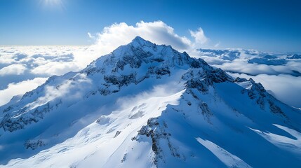 Naklejka premium Snow-covered mountain peak rises above clouds in a clear blue sky