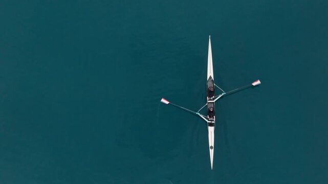 Two athletes rowing a sculling boat on calm blue water, teamwork and endurance in competitive sport. Rowers are practicing sport rowing. Rowers in a racing boat row in slow motion video 120fps.