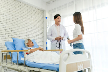Physician and caregiver consult beside elderly patient in hospital bed. Bright ward scene shows wellness, recovery, therapy, trust, stethoscope, practitioner care, monitoring, and teamwork support.
