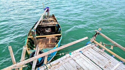 Traditional wooden fishing boat tied to a bamboo dock over green seawater. The old rustic vessel...