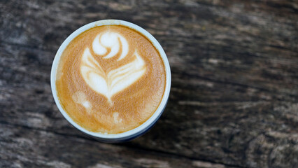 Cup of hot cappuccino with latte art on wooden table. Image in top view.