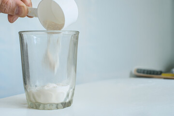 Man pouring protein powder into glass to make nutrition drink. Adding powdered dietary supplement into glass using white plastic scoop