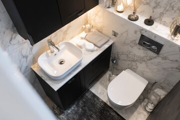Highangle view of a modern bathroom featuring a sleek sink toilet marble tiles and black cabinets