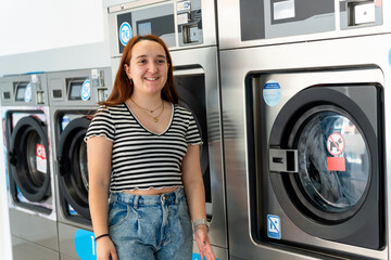Young woman smiling and washing clothes in laundromat