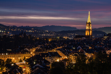 Fototapeta premium Bern, Switzerland, nighttime cityscape featuring illuminated buildings and a prominent tower, showcasing vibrant lights against a twilight sky, creating a serene urban atmosphere with captivating view