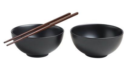 Pair of black ramen bowls in matte finish, chopsticks balanced above, one containing broth sheen while the other remains empty, isolated on transparent background.
