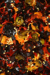 A detailed close-up of the remnants from cleaning roasted red sweet Macedonian peppers, with charred skin, seeds, and fleshy parts creating a rich texture