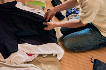 畳に座って洗濯物をたたむ男性の連続写真。家事をする男性。