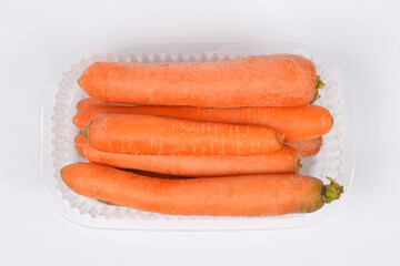 A top-down close-up view of a plastic container with fresh, unwashed carrots on a clean white background