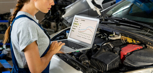 Female auto mechanic diagnostic car in repair shop using laptop