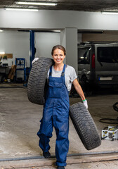 Young female tire shop worker smiling while carrying car tires. Woman at work. © Igor Barilo